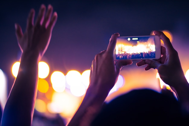 Fundo colorido embaçado da mão, segurando o telefone inteligente para tirar fotos pessoas lotadas em concerto.