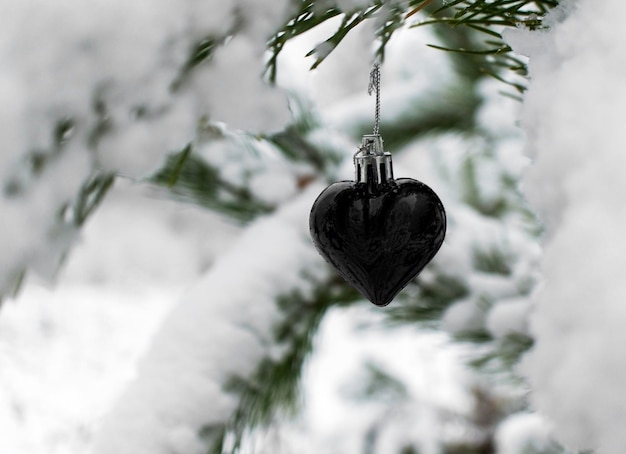 fundo com coração negro de brinquedo de árvore de Natal em galho de pinheiro coberto de neve no espaço de cópia de inverno