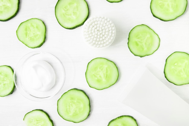 Fundo cosmético com fatias de pepino e produto cosmético de cor branca e escova de limpeza facial