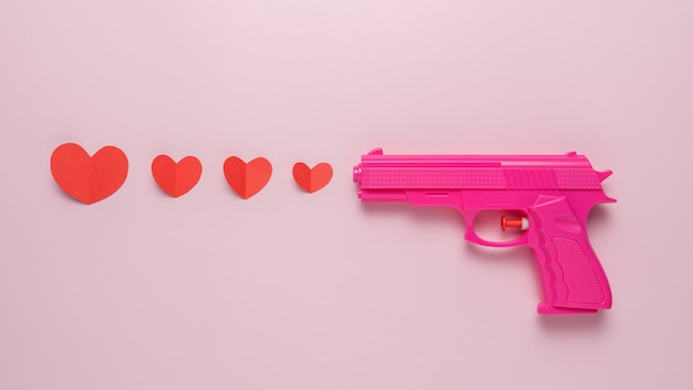 Fundo criativo feito com arma rosa e corações de papel vermelho