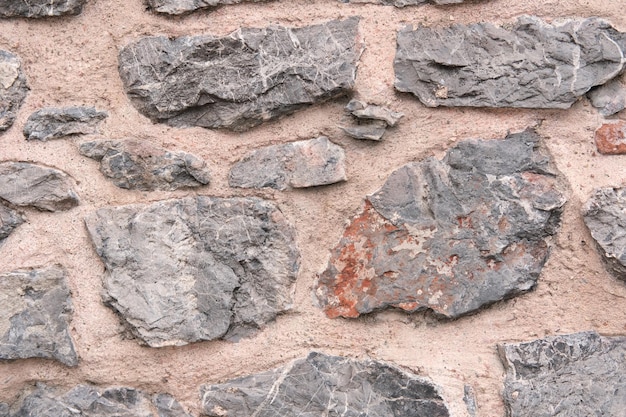 Fundo da parede de grandes pedras de mármore cinza e argila rosa com cimento e areia close-up