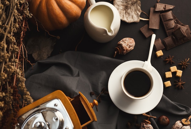 Fundo de café de outono de manhã. Xícara de americano, jarra de leite, moinho vintage, caqui seco, abóbora, vario e açúcar refinado na mesa rústica, copie o espaço