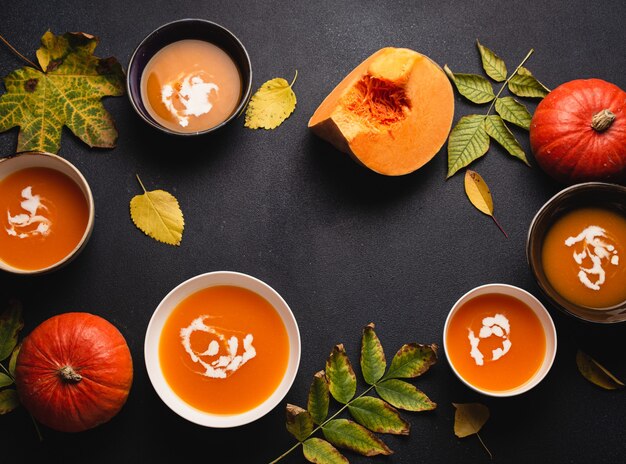 Fundo de comida com sopa de creme de abóbora caseiro aquecimento em pratos na mesa escura decorada com abóboras e folhas amarelas de outono. Conforto de outono com comida vegetariana saudável, vista de cima, espaço de cópia