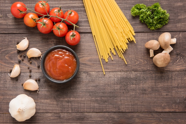 Fundo de comida italiana, com tomate, alho, pimenta, cogumelos e espaguete em fundo de madeira