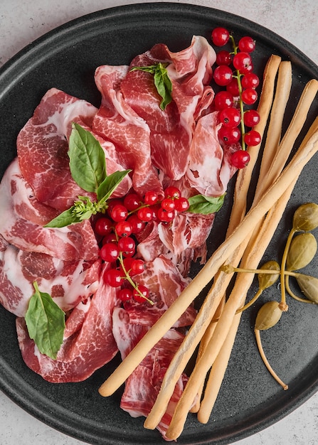 Fundo de comida presunto coppa di parma com manjericão grissini, alcaparras e groselha em