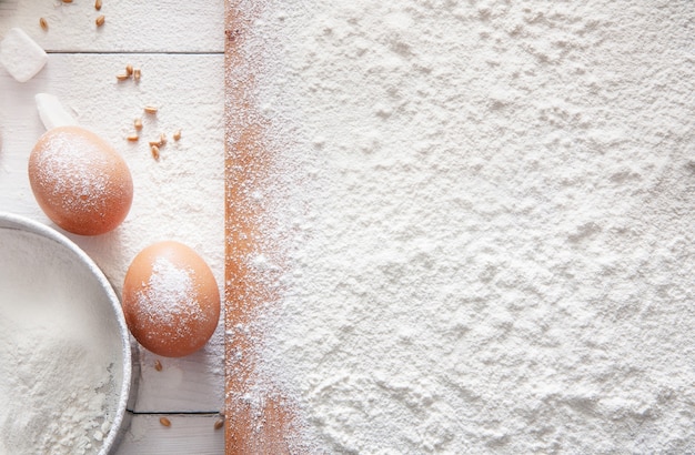 Fundo de conceito de classe ou receita de cozimento, ovos e farinha de trigo polvilhada na placa de madeira na mesa. Cozinhar massa ou pastelaria.