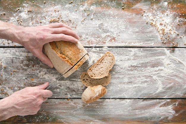 Fundo de cozimento. Mãos de padeiro cortando pão com faca na mesa de madeira rústica polvilhada com farinha.