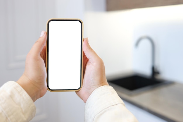 Fundo de cozinha com mão com telefone Cozinha doméstica turva com tela de smartphone em branco Conceito de pedidos de supermercado online Compras de comida online