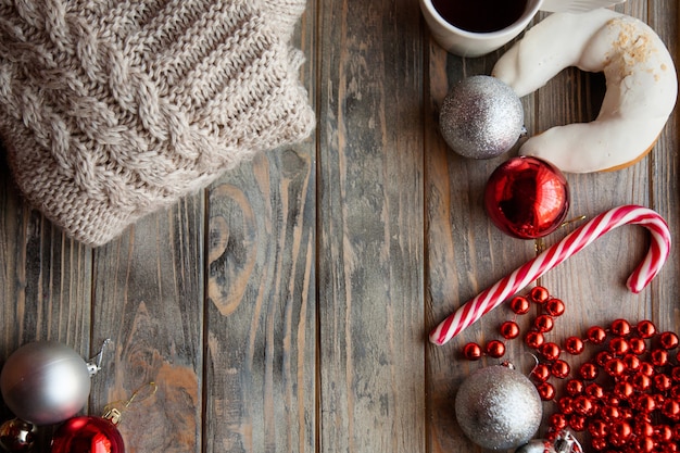 Fundo de decoração de Natal festivo. design sazonal com adornos e enfeites de férias. grânulos de bolas brilhantes de suéter de malha e bastão de doces em pano de fundo cinza de madeira.