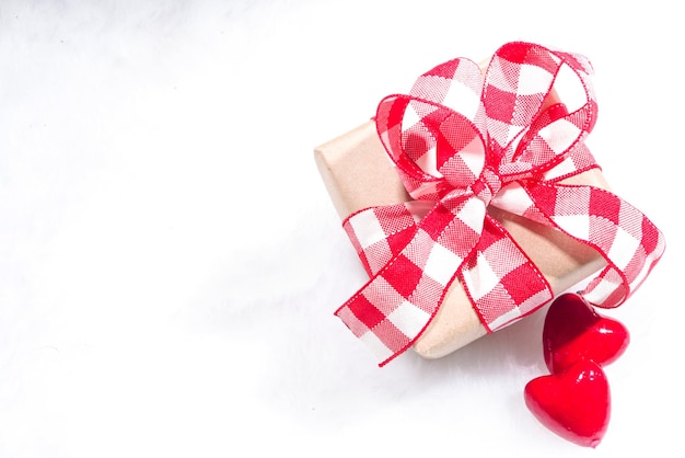 Fundo de feriado do dia dos namorados. Caixa de presente de papel artesanal com fita, decoração de flores rosas e corações, sobre fundo vermelho, vista superior, espaço de cópia