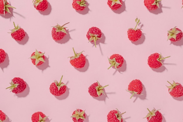 Foto fundo de frutas frescas com framboesas vermelhas maduras dispostas em um padrão aleatório em papel rosa em uma natureza morta plana