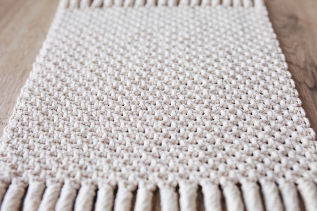 Foto fundo de macramé bege feito à mão. textura macramé, tricô ecológico, moderno. tapete macramê em mesa de madeira