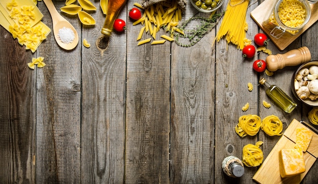 Fundo de massa. Vários tipos de massas secas com vegetais, queijos e ervas aromáticas. Em uma mesa de madeira. Espaço livre para texto. Vista do topo