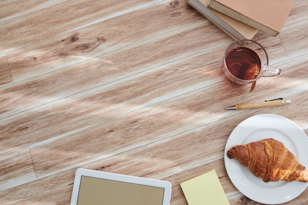 Fundo de mesa de escritório com uma xícara de chá e croissant, computador de mesa e livros