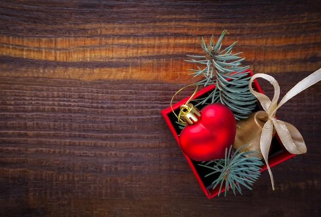 Fundo de Natal: caixa de presente vermelha com um brinquedo de Natal em forma de um coração, um sino de ouro e ramos de abeto