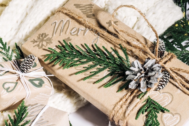 Foto fundo de natal com caixas de presente artesanais, cabos de corda e decorações com pinhas e twigson em fundo de madeira. preparação para férias. feito à mão. foco seletivo.