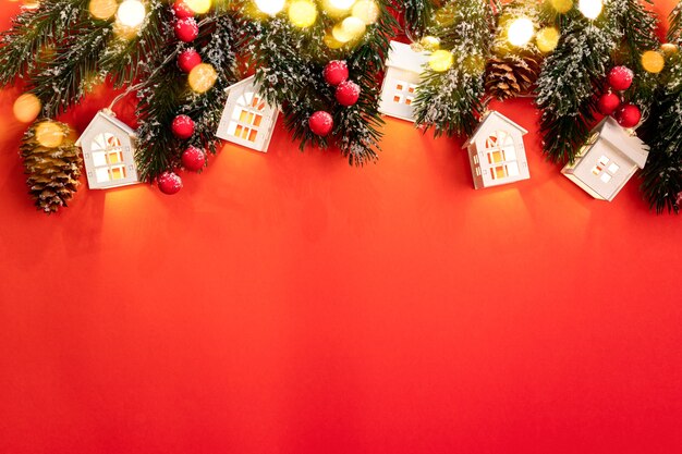 Fundo de natal com galhos de árvores de natal, luzes de natal luminosas, chalés brancos, bagas vermelhas e luzes brilhantes de bokeh no vermelho