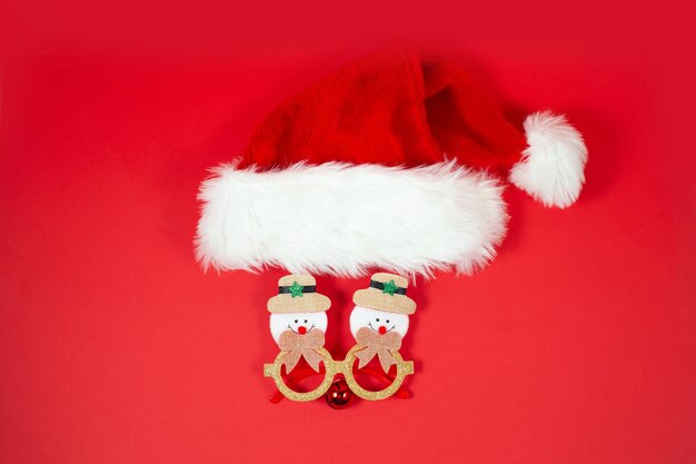 Fundo de natal festivo com chapéu de natal e óculos engraçados em um fundo vermelho. novo conceito normal de natal.