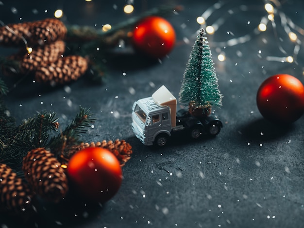 Fundo de Natal. Galhos de árvores de Natal com cones em um fundo escuro, bola vermelha, guirlanda e um caminhão com uma árvore de Natal