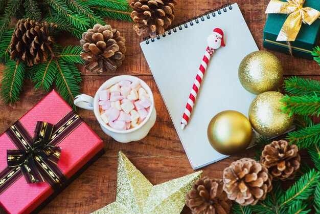 Fundo de Natal. Ramos de abeto, bolas de Natal, caderno e presentes e copo com marshmallows em um fundo de madeira. Copie o espaço Vista superior. Cartão de Natal ou Ano Novo. postura plana