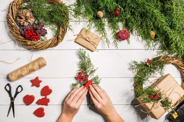 Fundo de Natal. Vista superior das mãos femininas embrulhe o presente de ano novo. Presentes embalados e pergaminhos, ramos de abeto e ferramentas na mesa de madeira. Local de trabalho para a preparação de decorações feitas à mão.