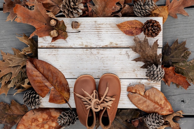 Fundo de outono com folhas naturais, pinhas e sapatos de couro em madeira envelhecida com espaço de cópia, conceito de férias de temporada