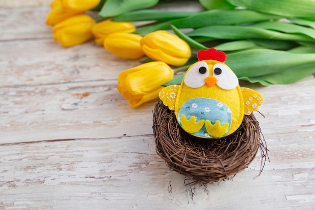 Fundo de páscoa com frango decorativo no ninho e tulipas amarelas em fundo de madeira