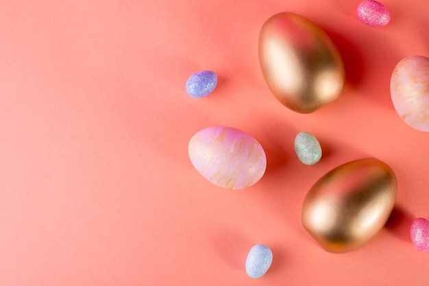 Fundo de Páscoa na moda com ouro e ovos de Páscoa coloridos em um fundo de cor coral claro com espaço de cópia Vista superior natureza morta Conceito de Páscoa