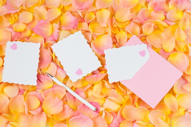 Fundo de pétalas de rosa cor de rosa, envelope rosa, corações, caneta e folhas de papel