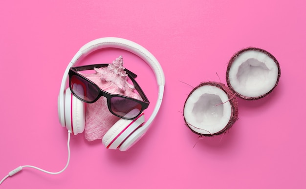 Fundo de praia de verão criativo. Férias na praia. Fones de ouvido, óculos de sol, coco, casca em fundo rosa. Vista do topo