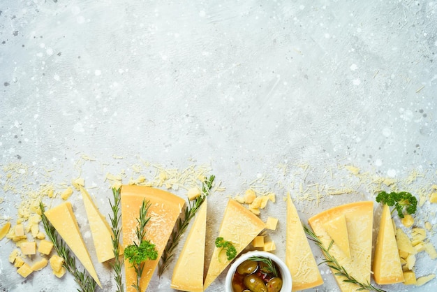 Fundo de queijo. Conjunto de queijos duros, azeitonas, alecrim e especiarias. Queijo parmesão duro. Vista do topo. Em um fundo de pedra.