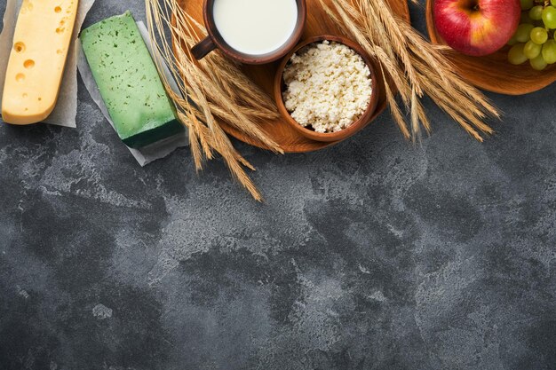 Fundo de shavuot feliz para celebração judaica religiosa tradicional de shavuot leite e queijo trigo maduro e frutas produtos lácteos sobre fundo cinza escuro antigo conceito de shavuot vista superior mock up