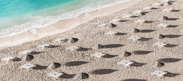 Foto fundo de verão com guarda-sóis e cadeiras de sol alinhadas na areia da praia com mar turquesa