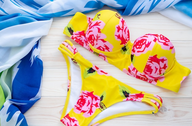 Fundo de verão com moda praia, biquíni amarelo e pareo azul sobre um fundo de madeira