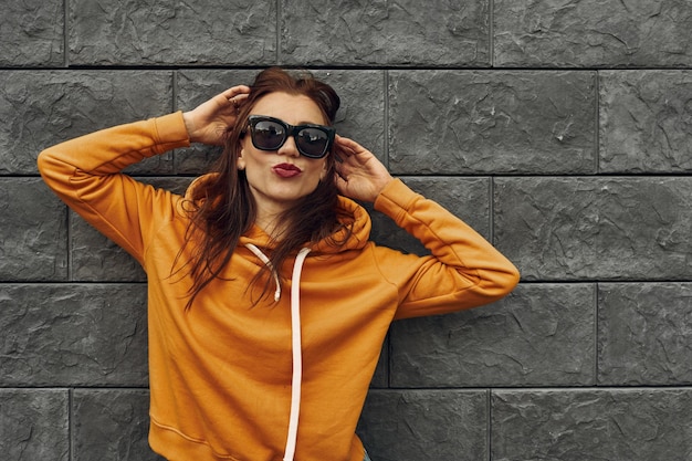 Fundo de verão. Linda garota com um capuz laranja contra uma parede cinza.