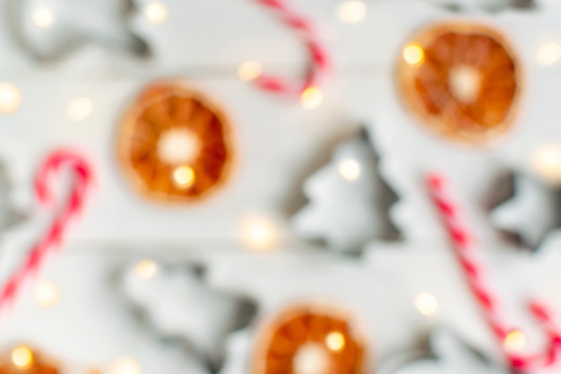 Fundo desfocado de Natal com bengala de doces, laranja seca e formas de cozimento na mesa de madeira branca com luzes brilhantes guirlanda.