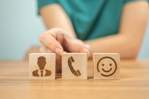 Fundo do conceito de serviço de call center Assistência e atendimento ao cliente e cooperação de suporte Cubos de madeira com ícones de sorriso e mão de jovem no escritório foto