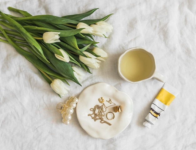 Foto fundo feminino joias de trajes um buquê de tulipas um clipe de cabelo creme de mão chá verde acessórios de beleza estética em um fundo claro vista superior