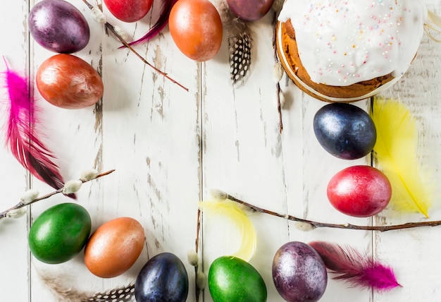 Fundo festivo da Páscoa. um bolo com glacê, penas e ovos coloridos, raminhos de salgueiro em uma mesa de madeira branca.