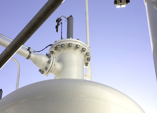 Foto fundo industrial com tubos, juntas, parafusos e tanque de pressão de cor branca com céu azul como fundo