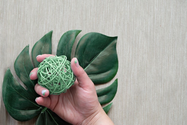 Fundo mínimo tropical exótico com mãos bem cuidadas segurando uma bola de rattan Flat lay on moody