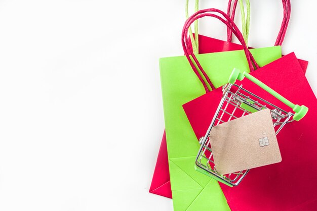 Fundo preto sexta-feira de venda de Natal com sacolas de papel verde vermelho, carrinho de compras, smartphone, cartão de banco no espaço de cópia de fundo branco