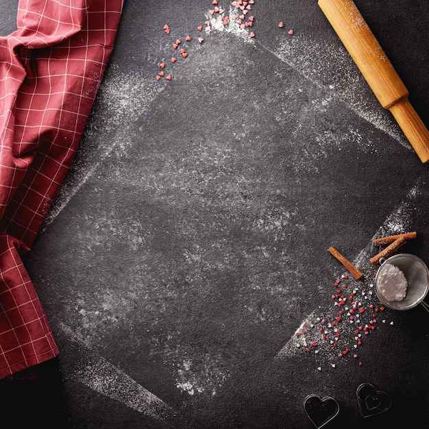 Foto fundo preto vertical polvilhado com farinha e açúcar de confeiteiro e com utensílios de cozinha