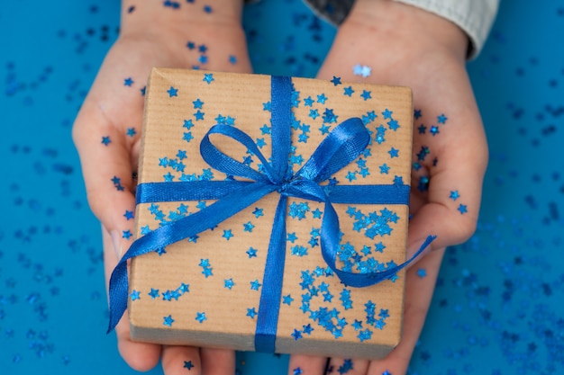 Funkelnde Geschenkbox in Bastelpapier eingewickelt und mit Schleife in Kinderhänden gebunden