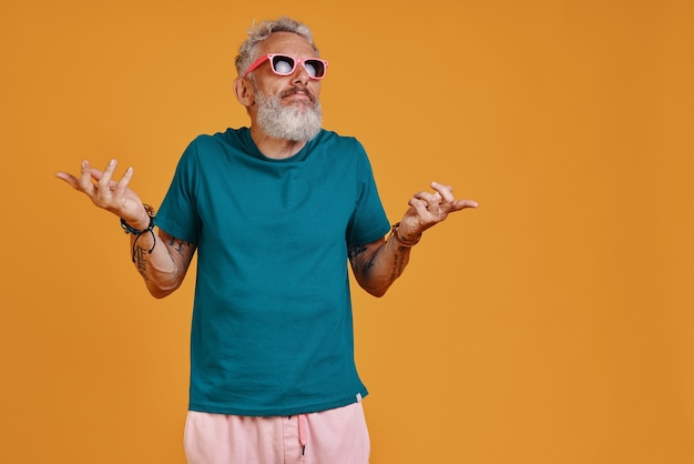 Funky senior hombre encogiéndose de hombros mientras está de pie contra el fondo naranja