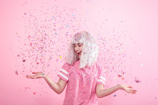 Funny Girl con cabello plateado da una sonrisa y emoción en la pared rosa. Joven mujer o niña adolescente con confeti