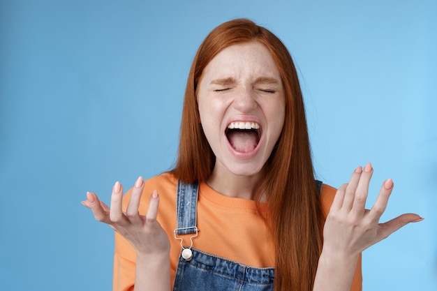 Furiosa, indignada e temperamental garota ruiva gritando reclamando com raiva em pé incomodado gritando bem alto feche olhos gritando bem alto levantando as mãos para o lado desânimo total descrença sentir traição dolorosa traição