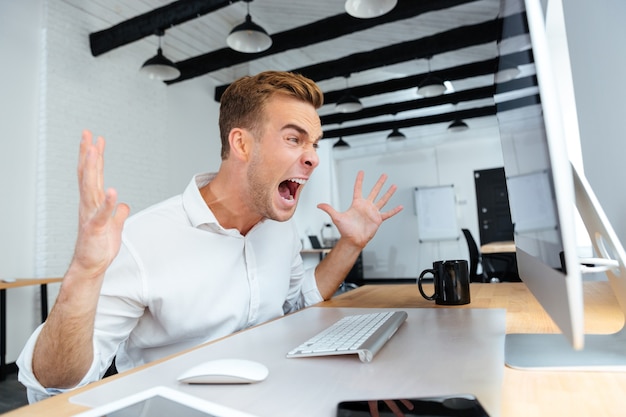 Foto furioso e zangado jovem empresário trabalhando com computador e gritando