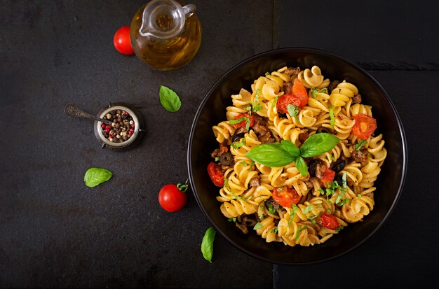 Fusilli da massa com tomates, carne e manjericão na bacia preta na tabela.