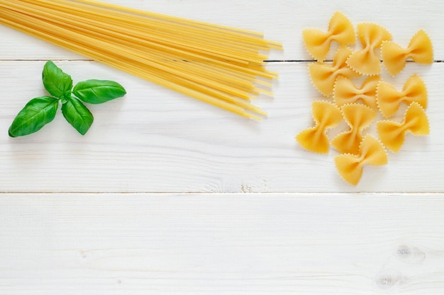 Fusilli espagueti pasta cruda hoja de albahaca sobre tablero de madera blanca fondo vista superior espacio para copiar texto